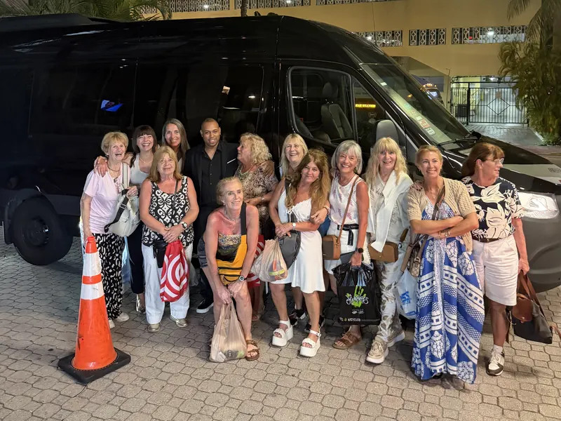 Group of Cruise Shuttle Miami riders posing in front of the black Mercedes Sprinter at a hotel pickup at night